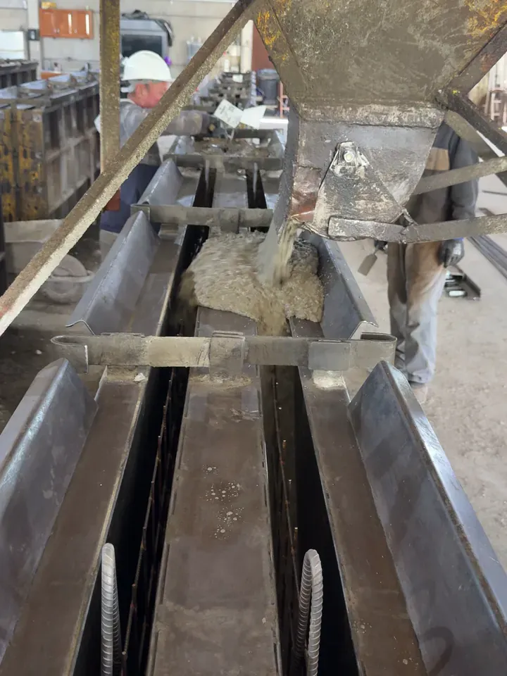 Concreto descendo da caçamba para dentro da forma metálica, com a armadura na forma e a equipe da Gemold ao fundo